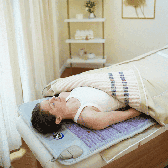 Woman relaxing on a massage bed with a heated blanket.