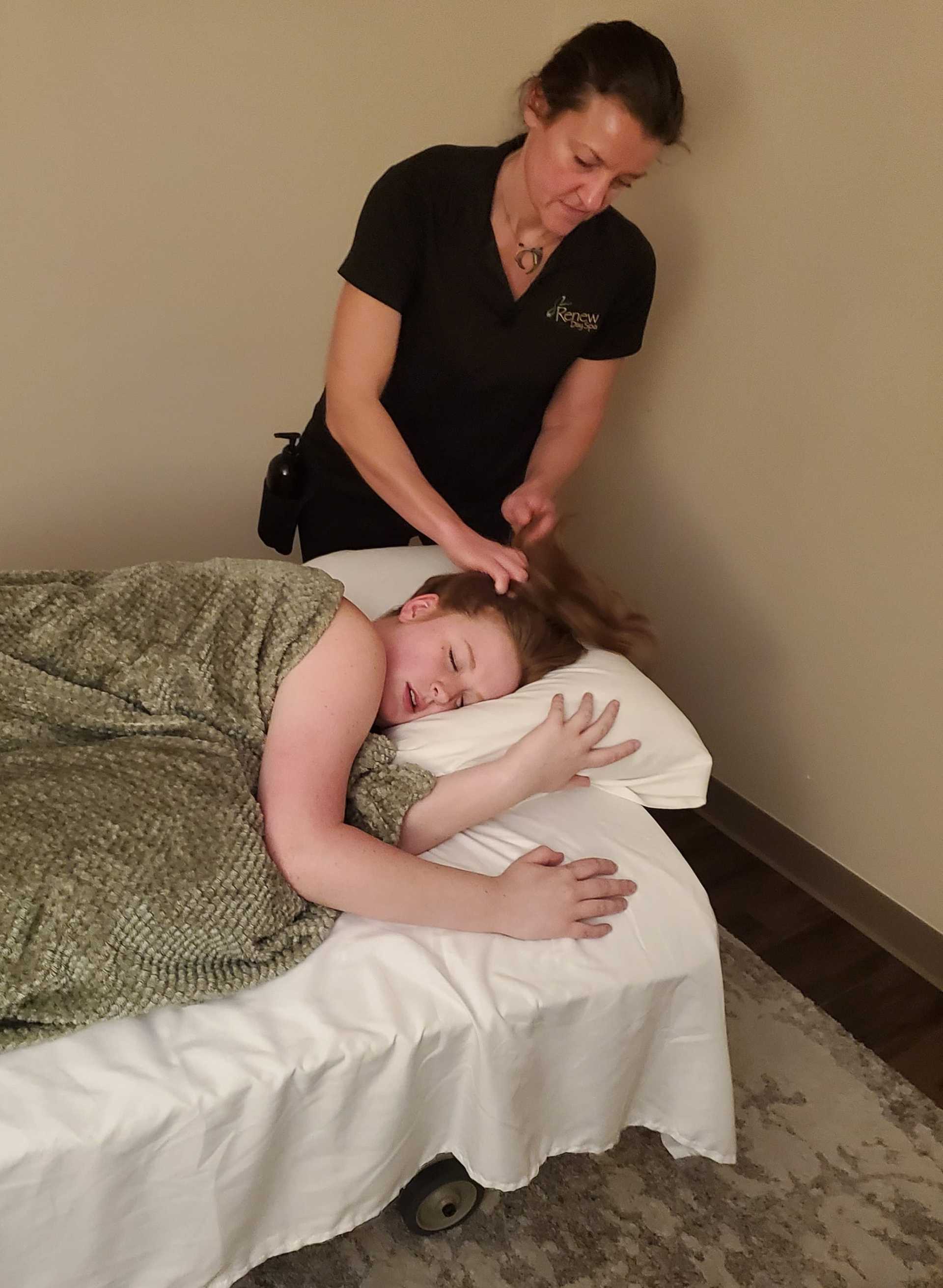 Massage therapist working on client's scalp while lying on a massage table.