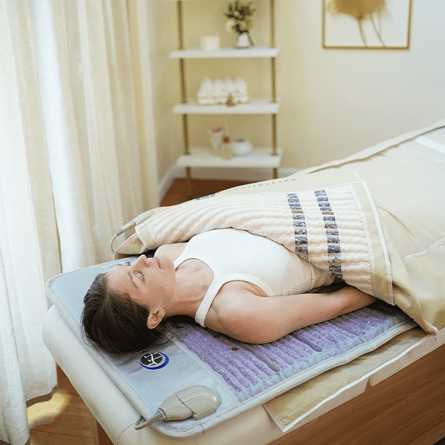 Woman relaxing on a massage bed with a heated blanket.
