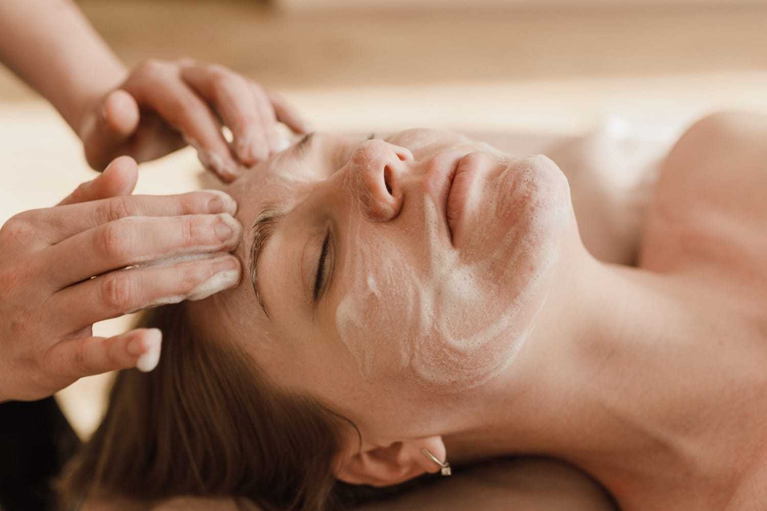Facial massage being performed on a relaxed person with a cleansing mask.